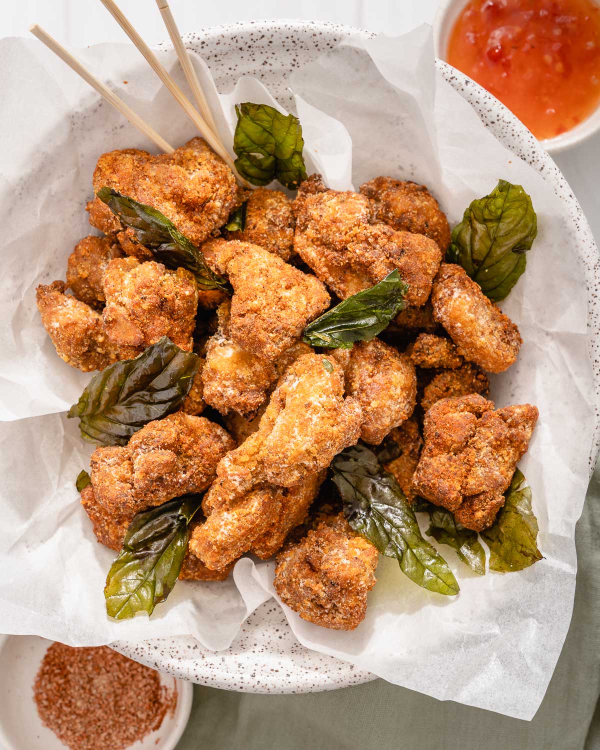 Looking down into a bowl of Taiwanese fried chicken with fried basil and skewers for eating.