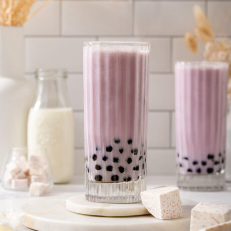 Two glasses of taro milk tea with boba on a counter.