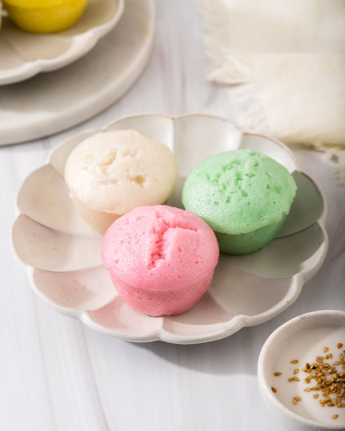 Three colorful Bánh Bò Hấp sitting on a petal shaped plate.
