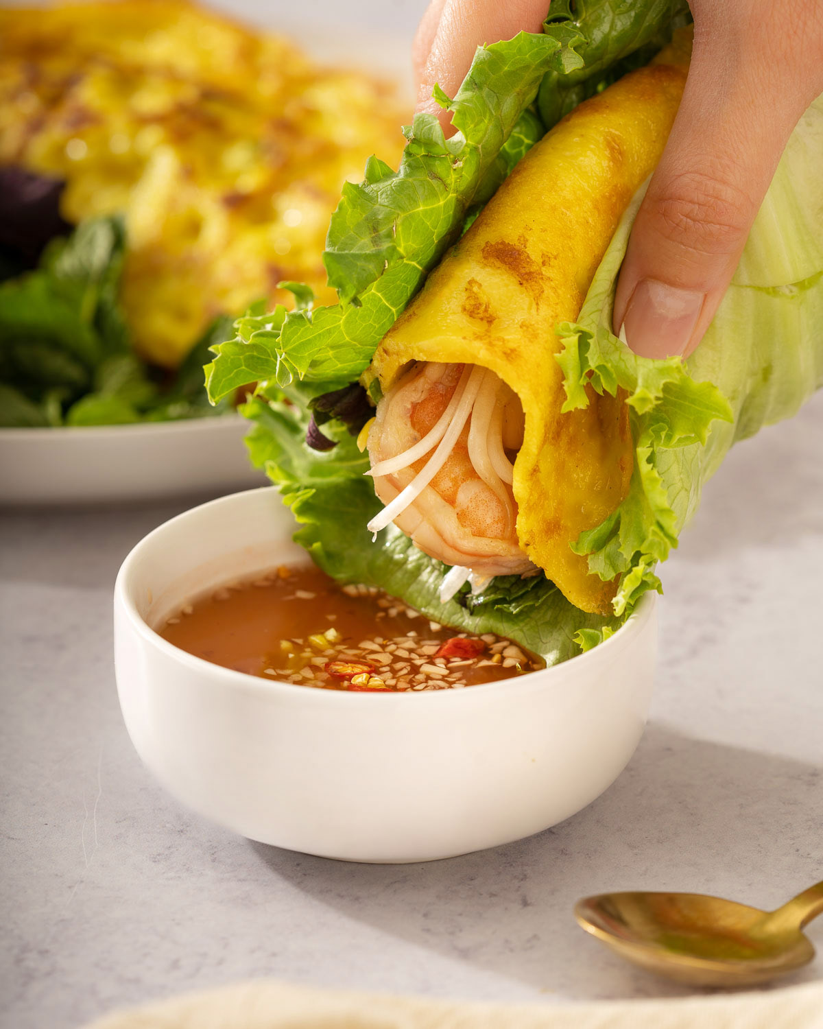 Dipping a bánh xèo wrapped in lettuce into Vietnamese dipping sauce.