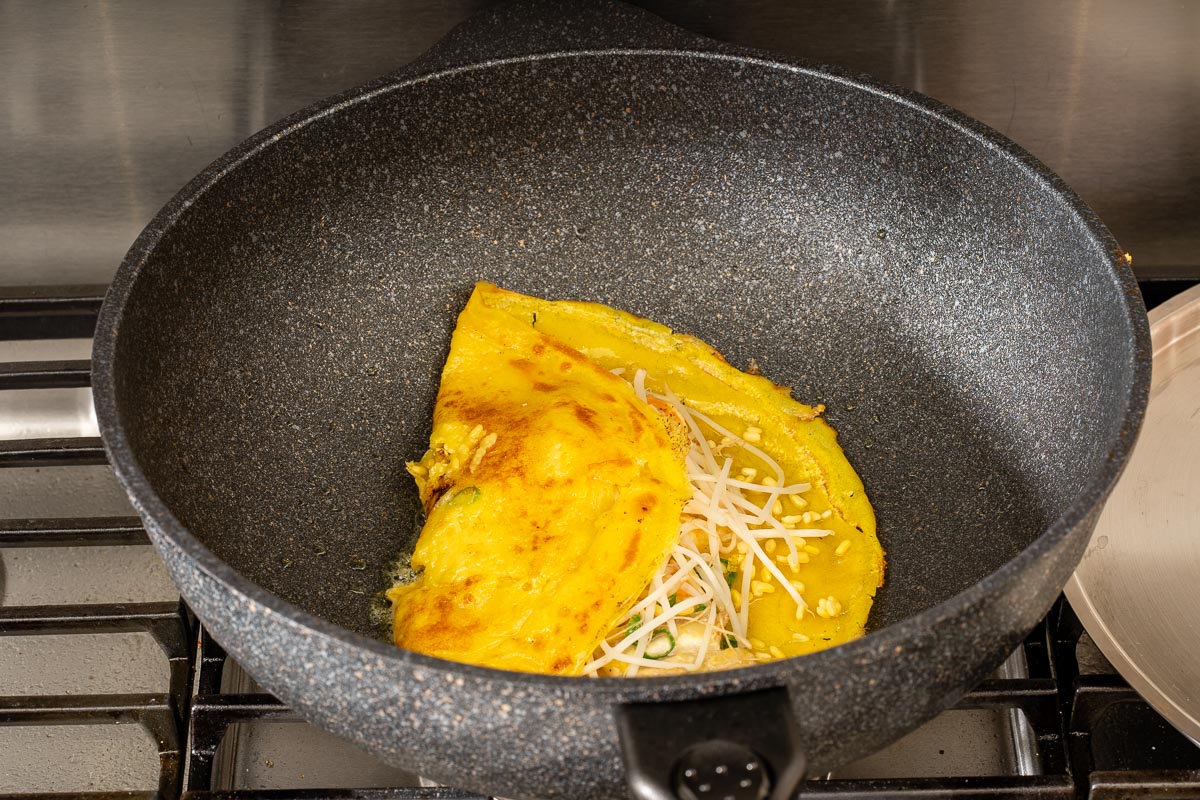 Folding half of the banh xeo over to finish cooking the crepe.