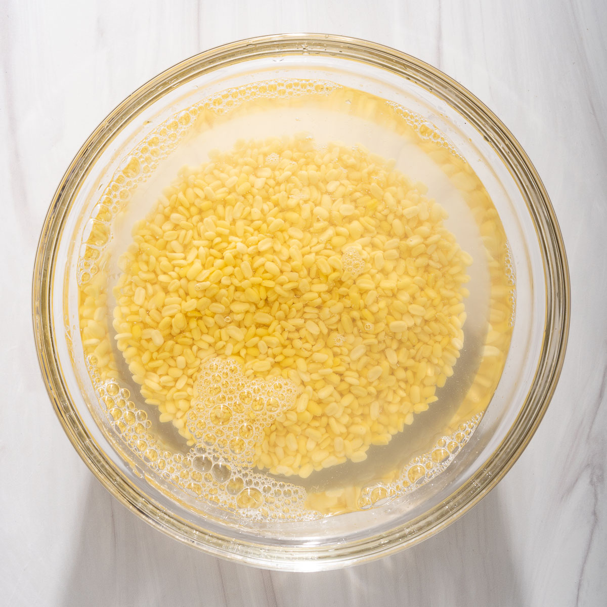 Mung beans soaking in a glass bowl full of water.
