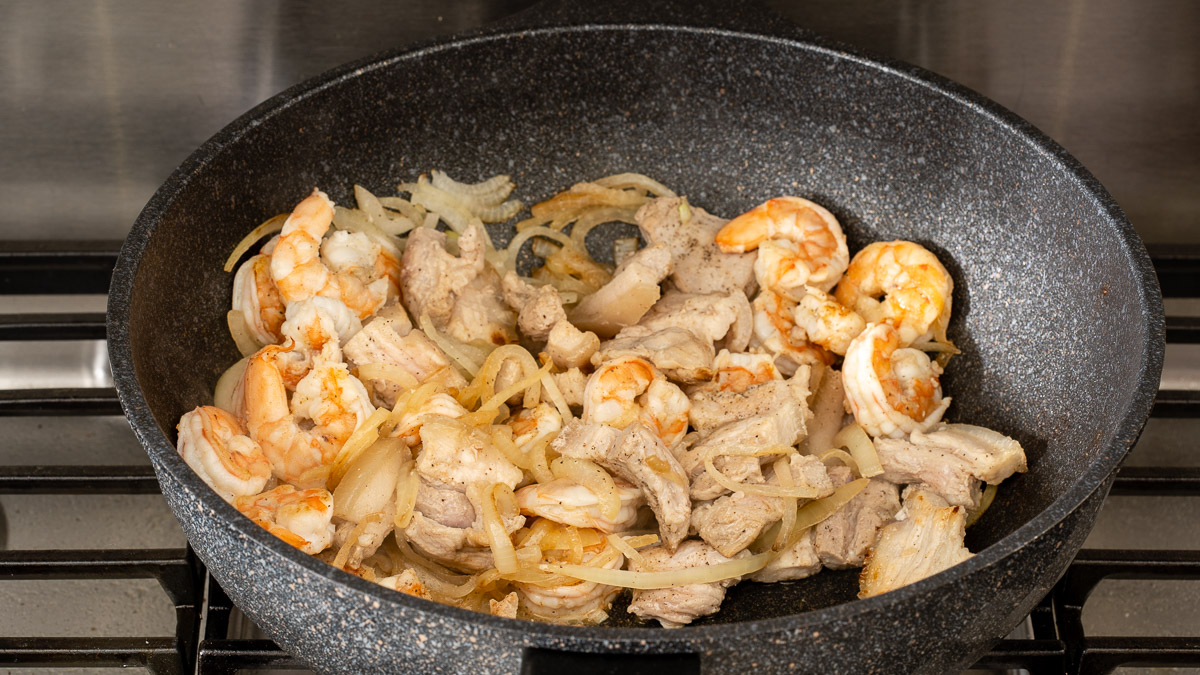 Various proteins being tossed together inside a large wok on the stove.
