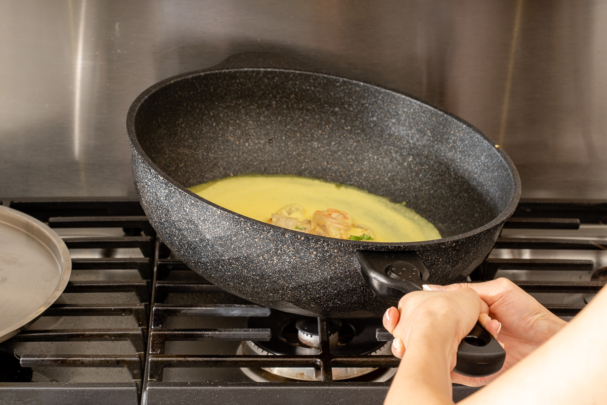 Tilting and swirling the bánh xèo batter to create an even thin layer crepe.