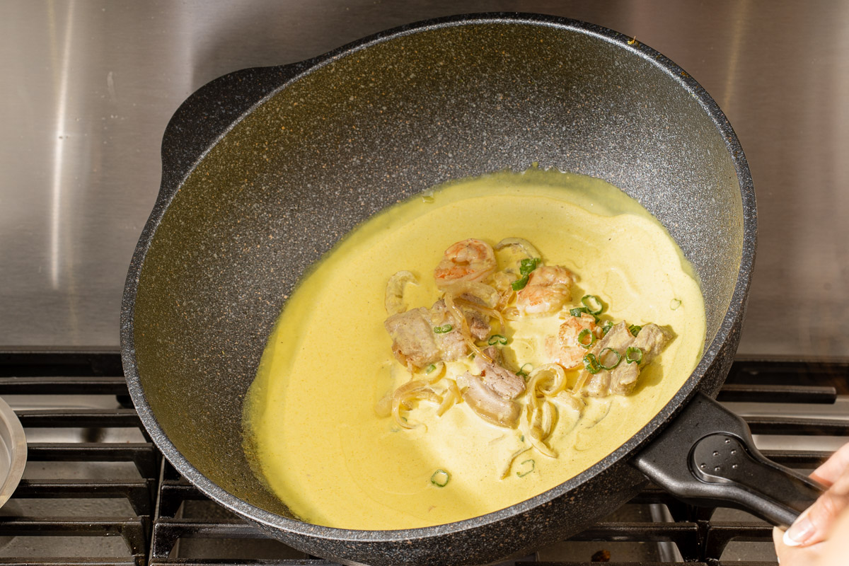 Tilting and swirling the bánh xèo batter to create an even thin layer crepe.