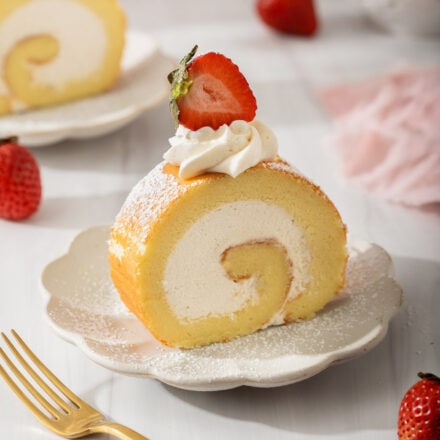 Up close of a slice of Japanese roll cake dusted with sugar and strawberries.