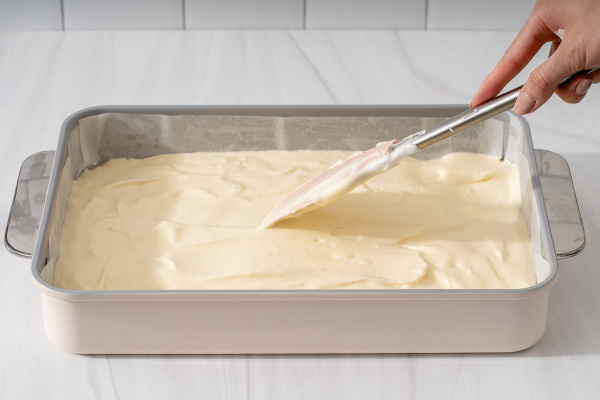 Spreading roll cake batter evenly across the bottom of a lined tray.