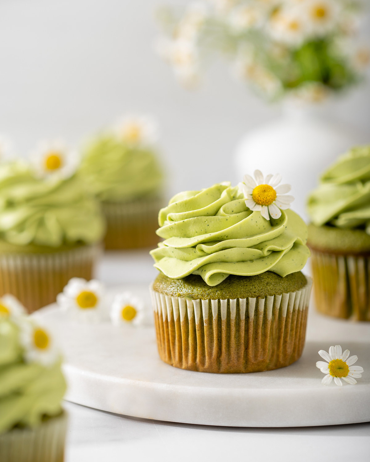 A matcha cupcake on a marble tray surrounded by more matcha cupcakes.
