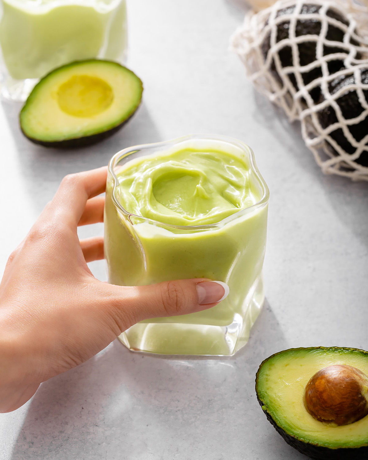 Someone grabbing a glass of avocado smoothie from a countertop.