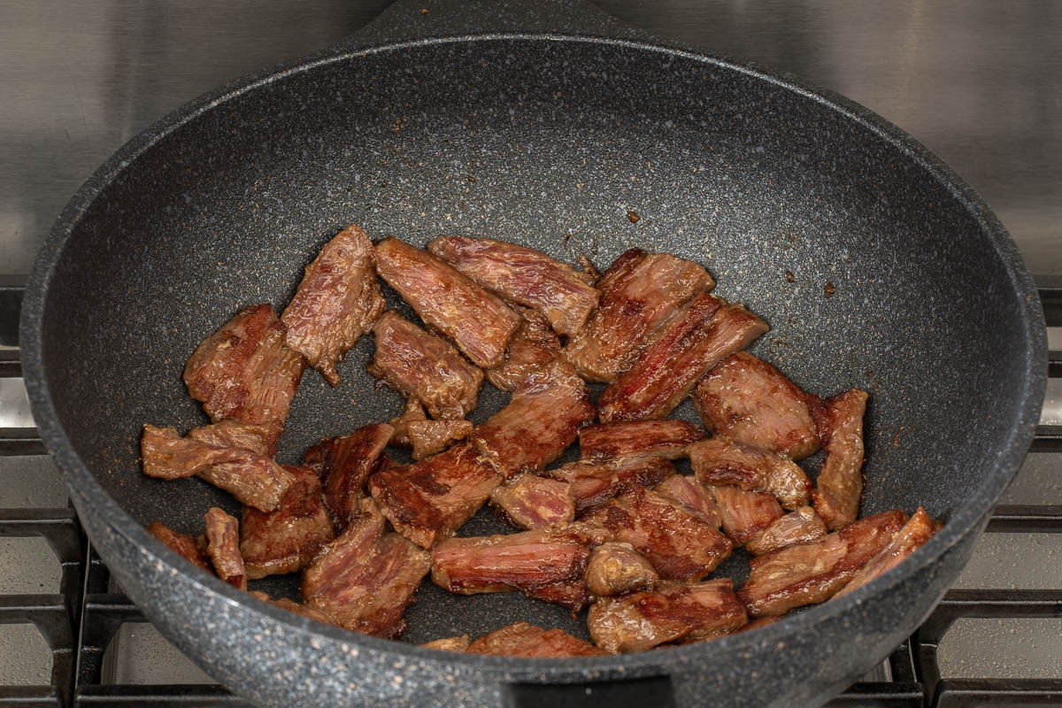 Cooking the marinated sliced beef in a large wok on the stove.