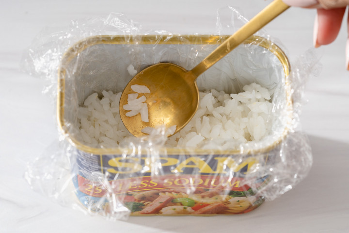 Pressing sushi rice inside a plastic wrapped lined empty spam can.