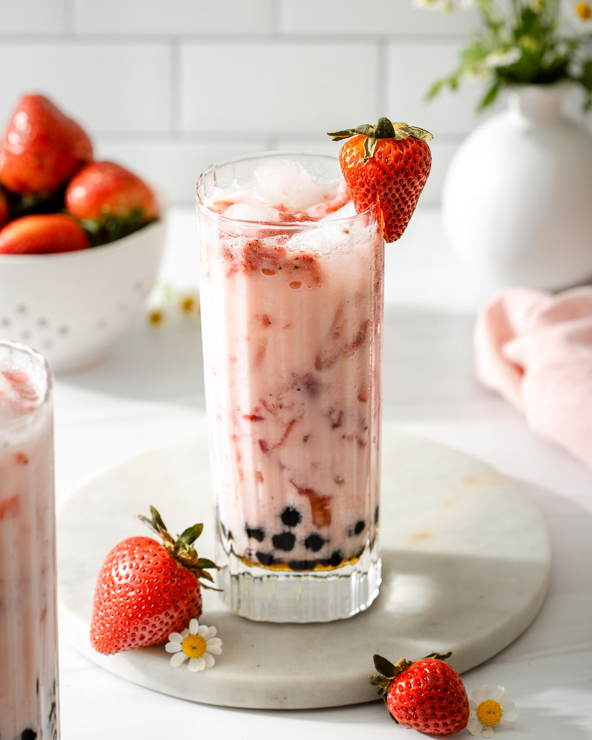 A tall glass of strawberry milk tea with boba on a serving tray with fresh strawberries.