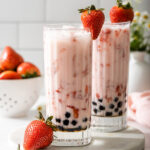 Up close of two glasses of strawberry milk tea with boba and fresh strawberries.