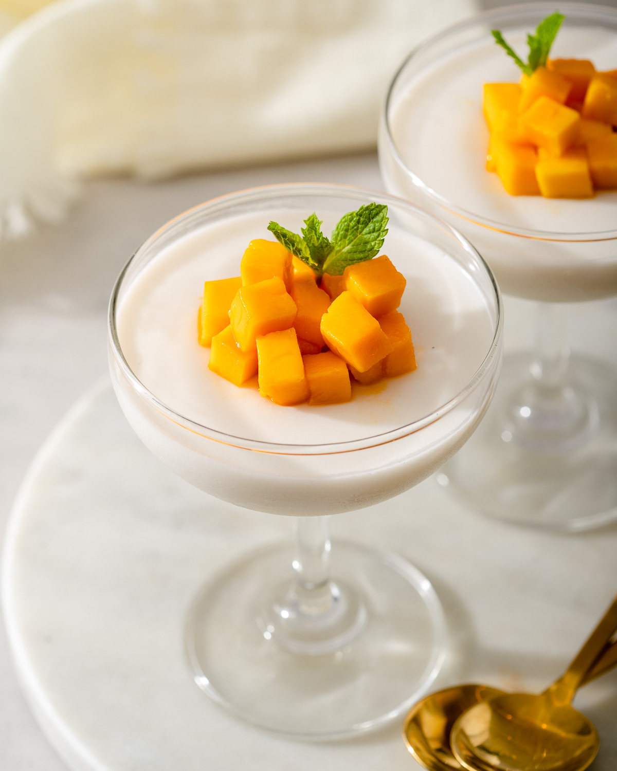 Two coupe glasses with coconut jelly topped with chopped mango.