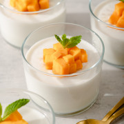 Several small glasses full of coconut jelly and mango with spoons nearby.