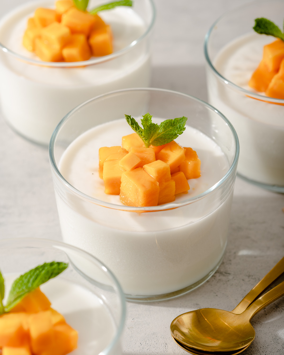 Several small glasses full of coconut jelly and mango with spoons nearby.