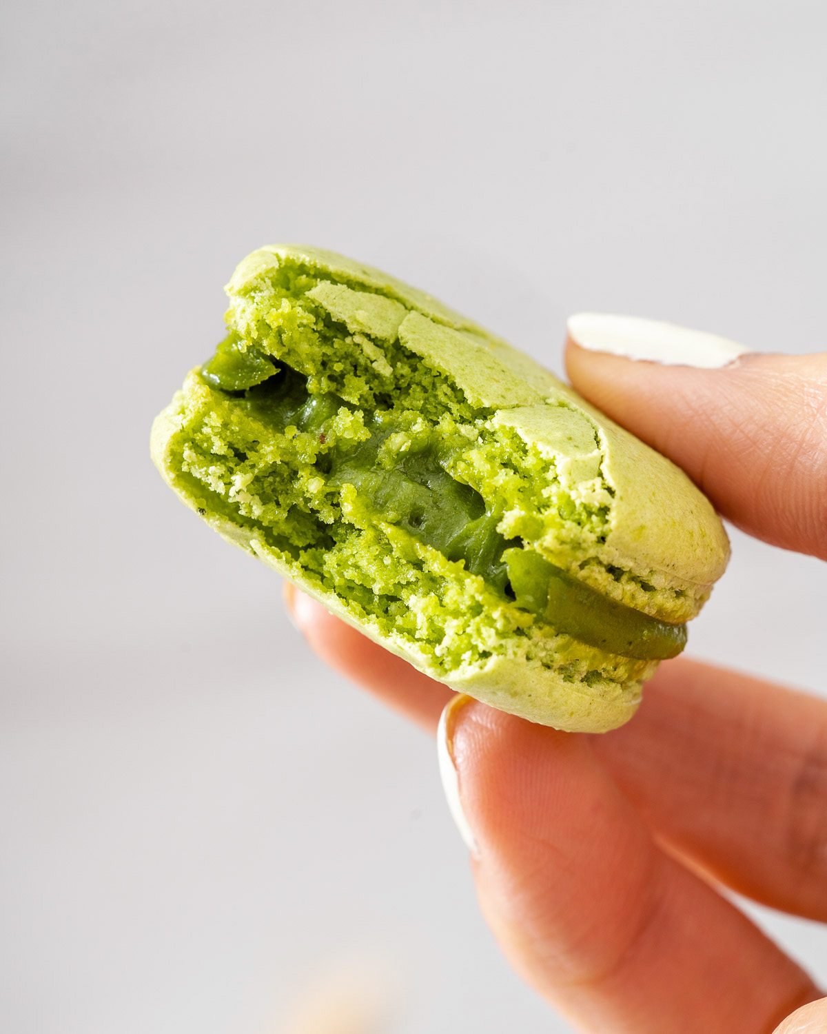 Holding a bitten matcha macaron up close to see the ganache filling.