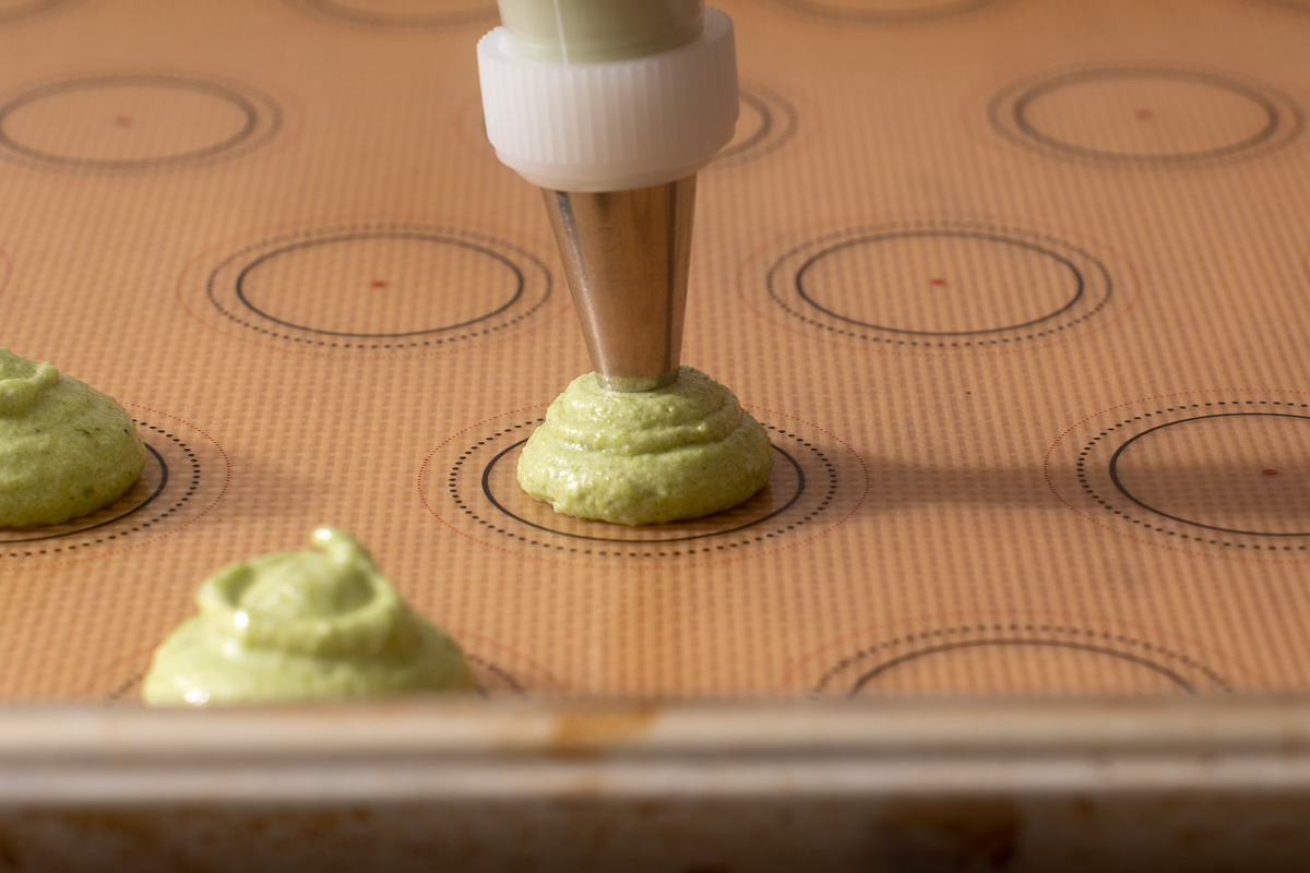 Piping the batter onto a silicone mat lined tray with a macaron template.