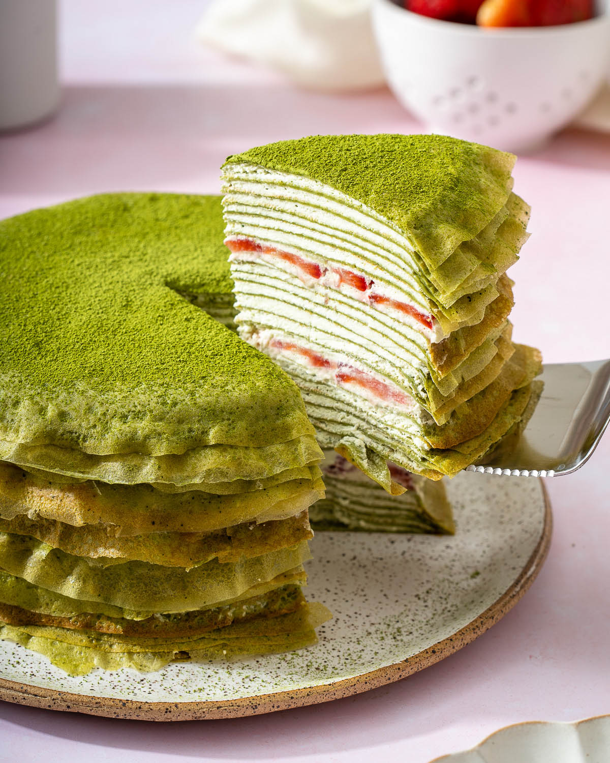 Someone lifting slice of cake from a matcha crepe cake.