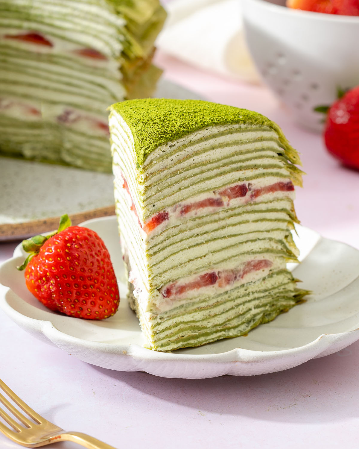 Up close of a slice of matcha crepe cake on a plate with a strawberry.