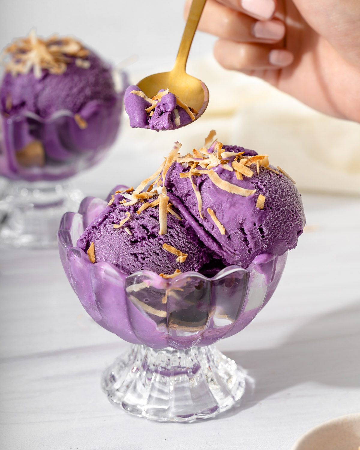 Someone lifting up a spoonful of ube ice cream from a small glass dish.