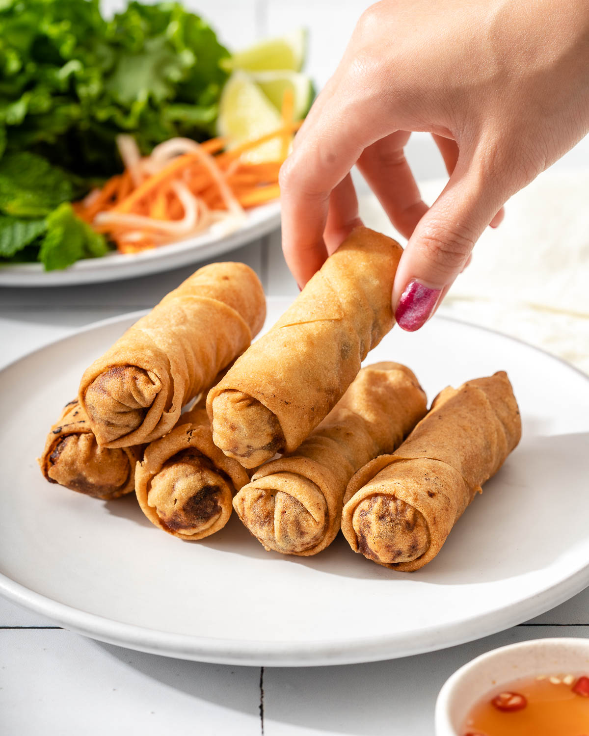Someone grabbing an egg roll from a plate piled with egg rolls.