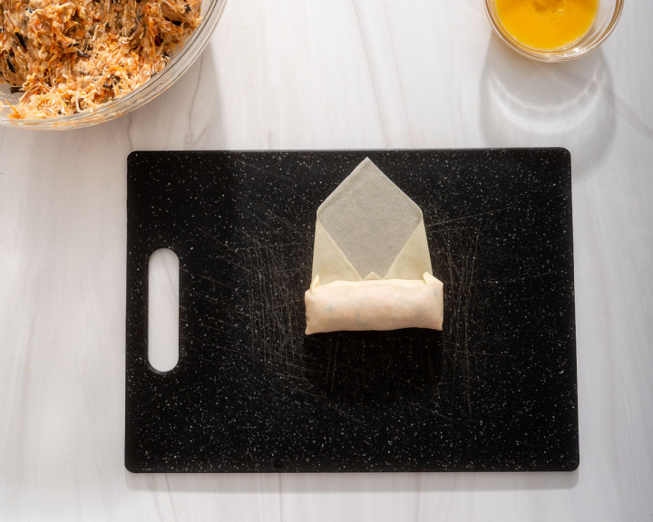 Rolling the egg roll wrapper tightly.