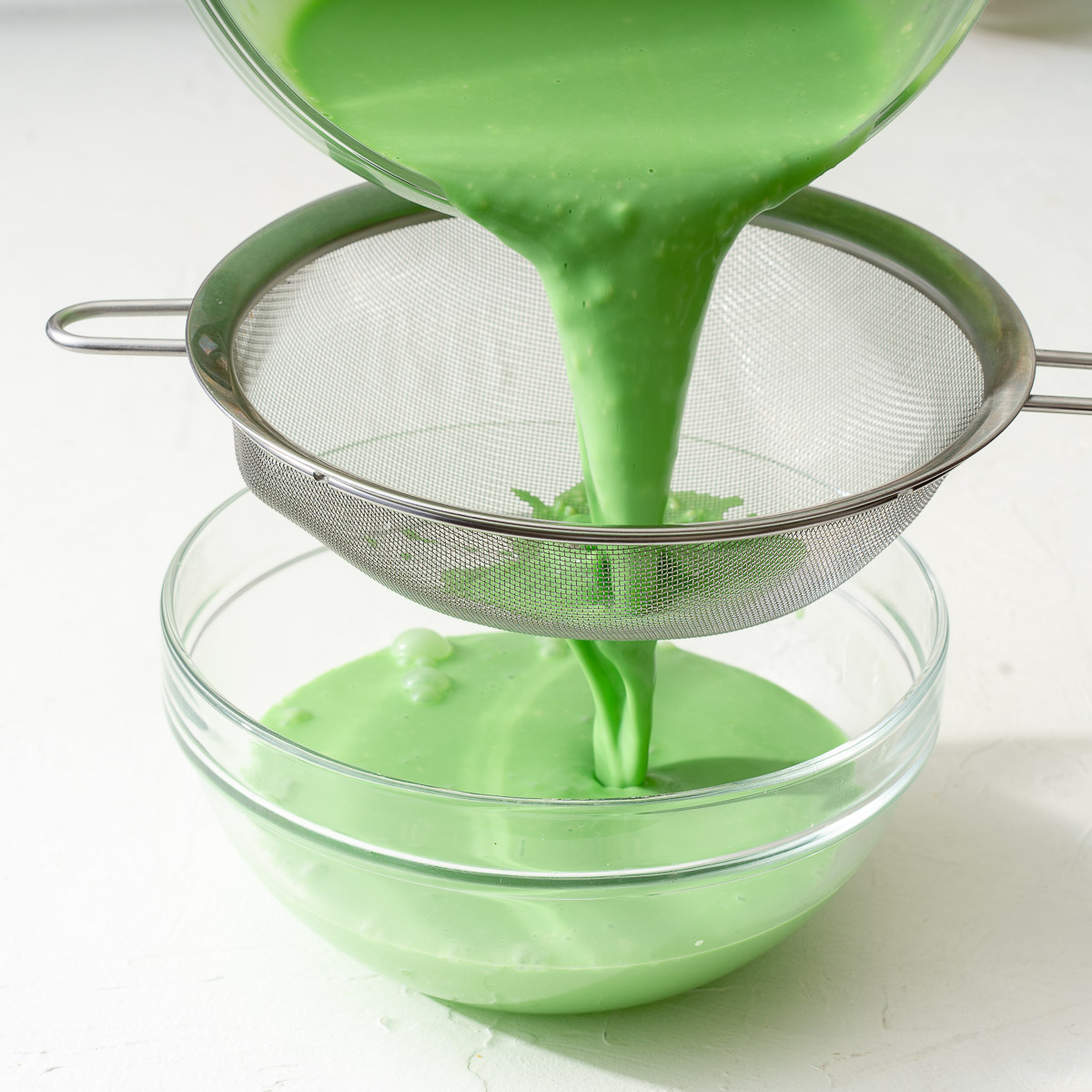 Sifting the combined heavy cream and pandan through a fine mesh sieve.