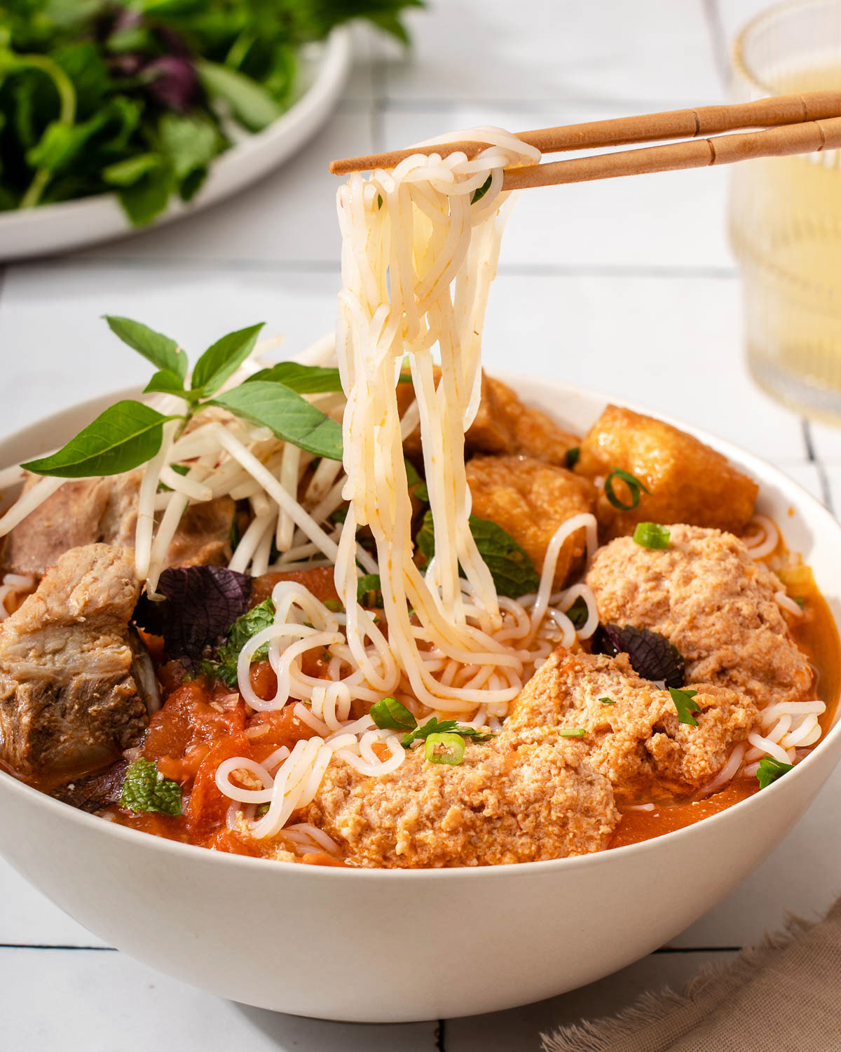 Someone lifting noodles with chopsticks from a bowl of Vietnamese bun rieu.