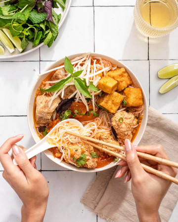 Looking down at a person eating a bowl of Vietnamese crab and tomato soup.