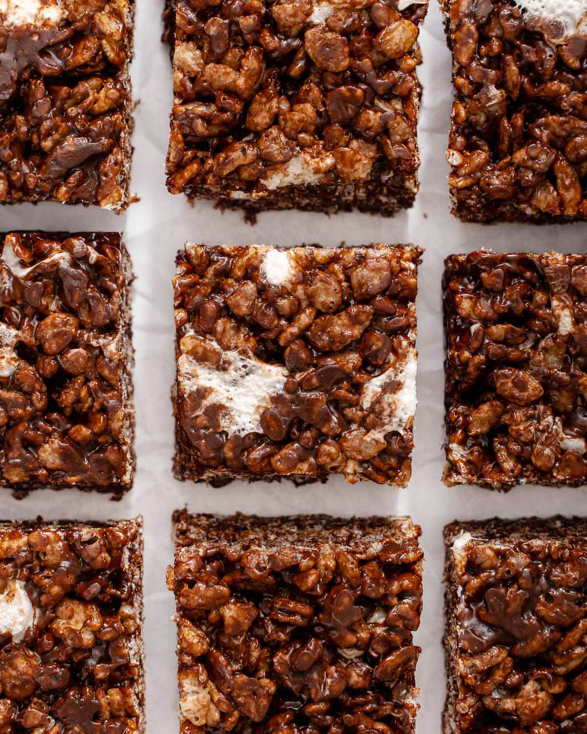 Up close of a grid of chocolate rice krispie treats on parchment paper.