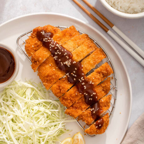 Up close of a plate with sliced chicken katsu with sauce and cabbage nearby.