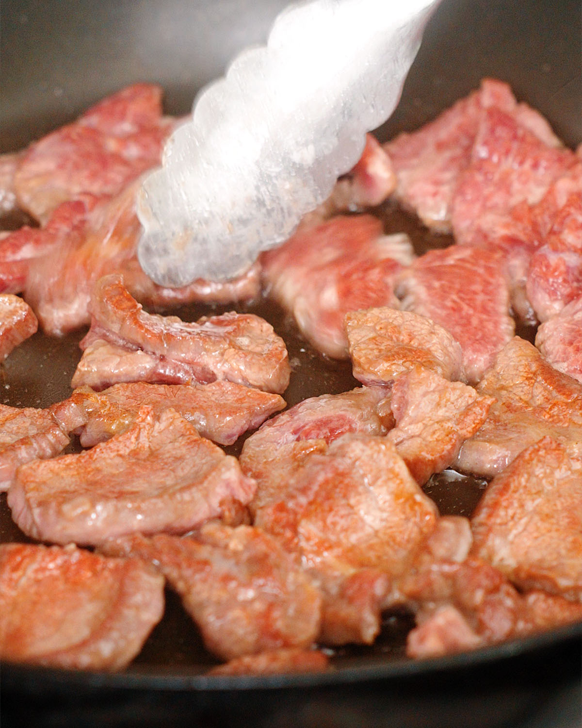 Turning over the sliced beef in the pan to sear each side.