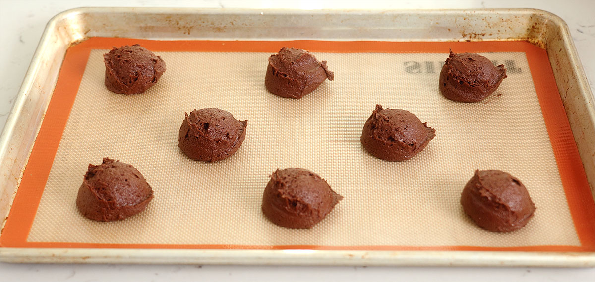 The balls of fudgy peppermint brownie cookie dough spaced apart on a lined baking tray.