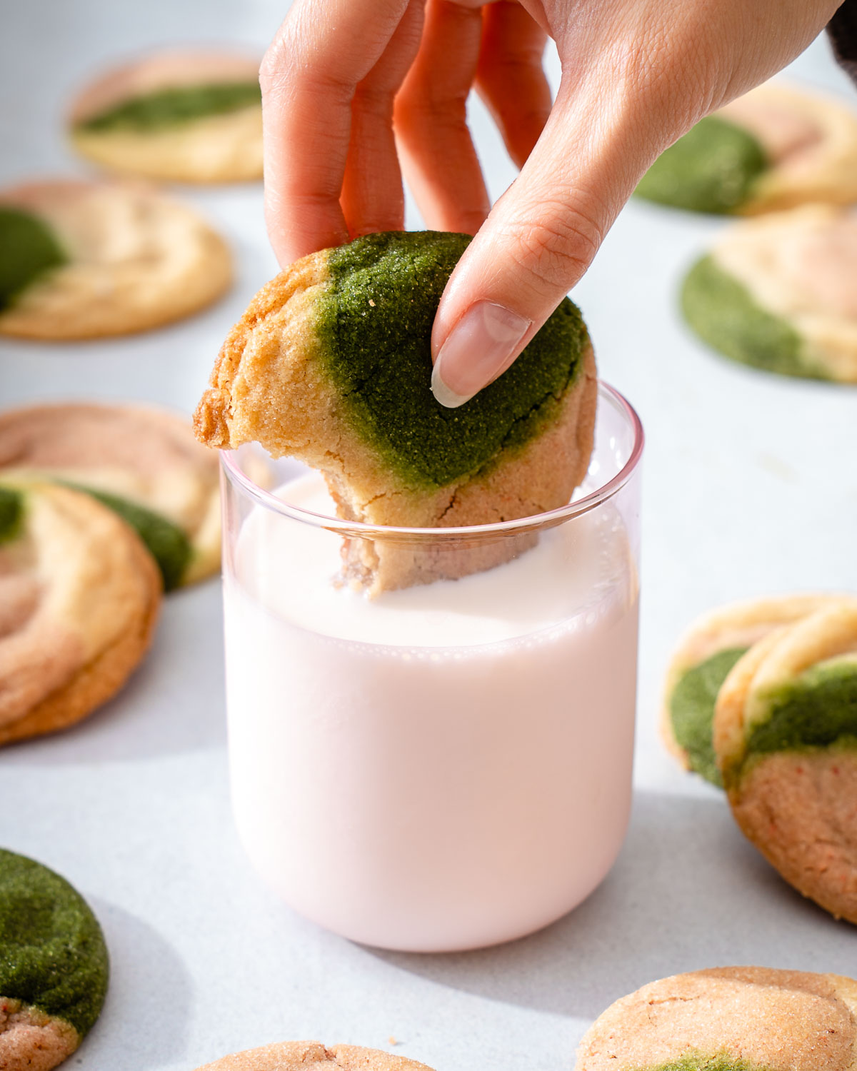 Dipping a strawberry matcha neapolitan cooked in milk with several cookies nearby.
