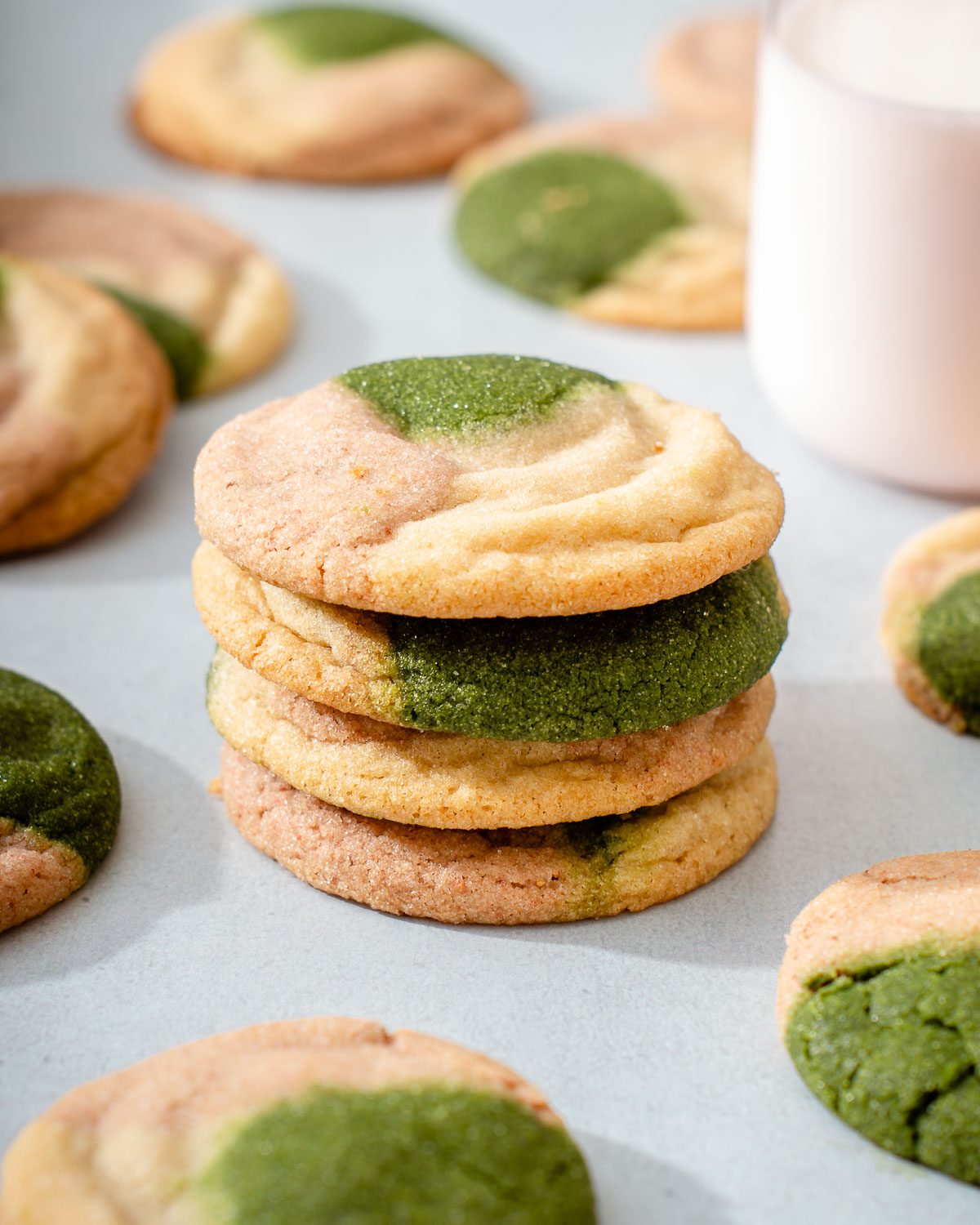 A stack of strawberry matcha neapolitan cookies with a glass of milk nearby.