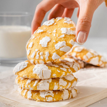 Someone lifting up a yuzu lemon crinkle cookie from a stack of cookies.