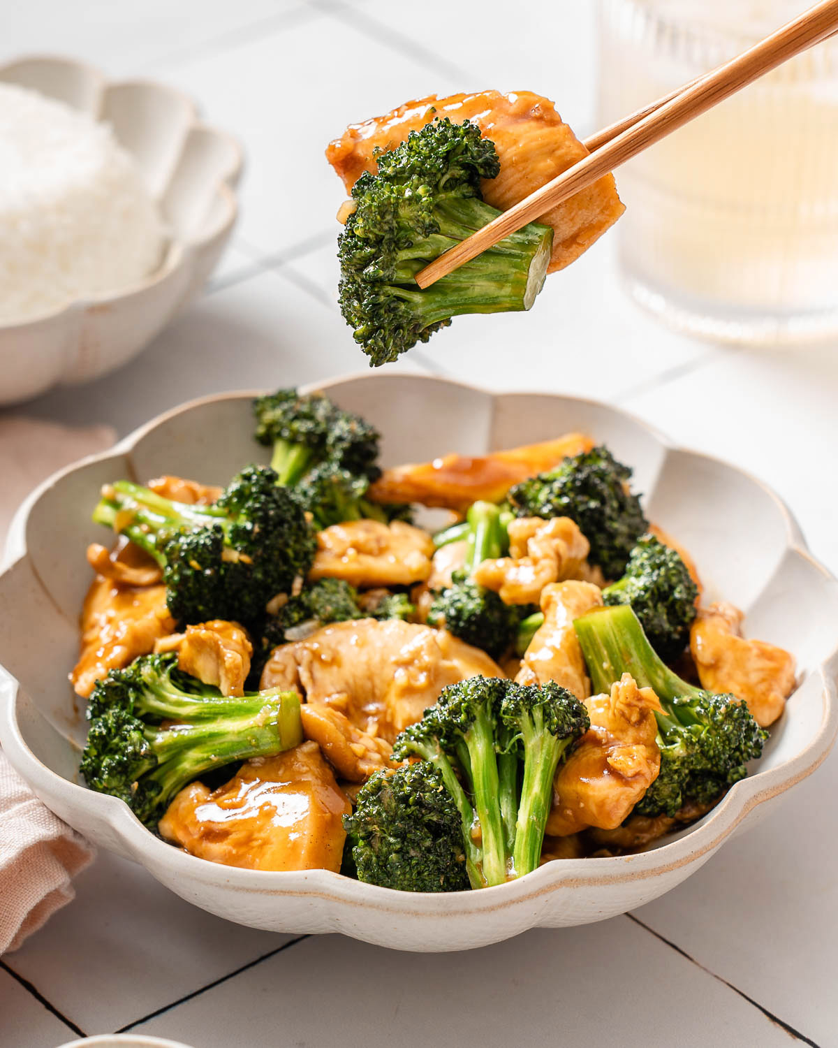 A pair of chopsticks lifting up chicken and broccoli from a bowl of Chinese chicken and broccoli.