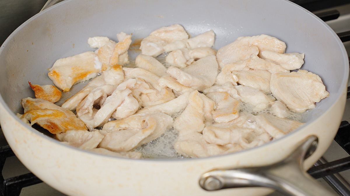 Cooking the sliced chicken breast in a large pan.