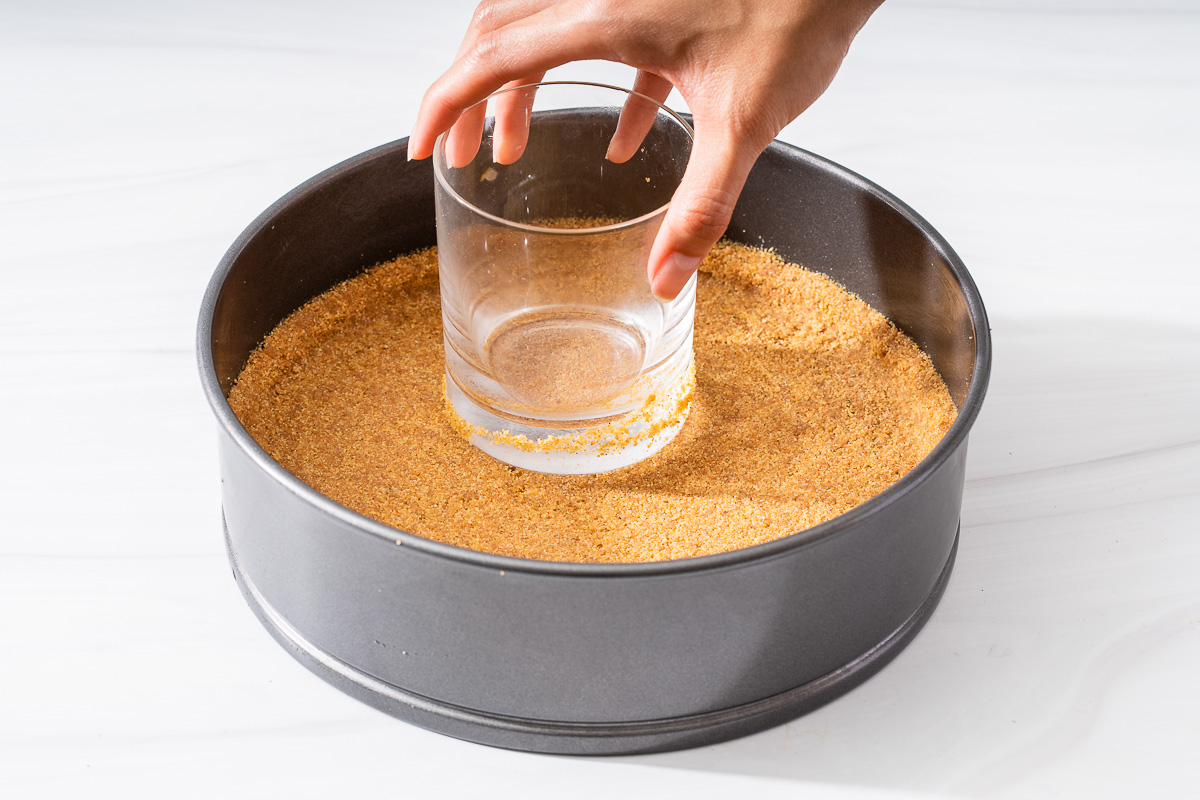 Pressing the graham cracker crust into the round pan with a flat bottomed glass.