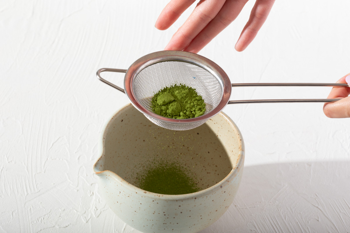 Sifting ceremonial matcha with a fine mesh strainer into a matcha bowl.