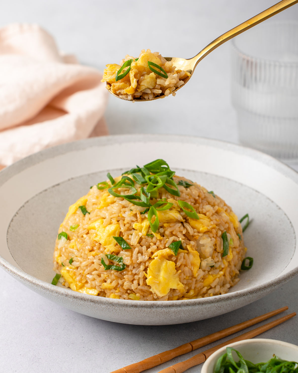 A spoonful of rice being lifted from a bowl of egg fried rice.