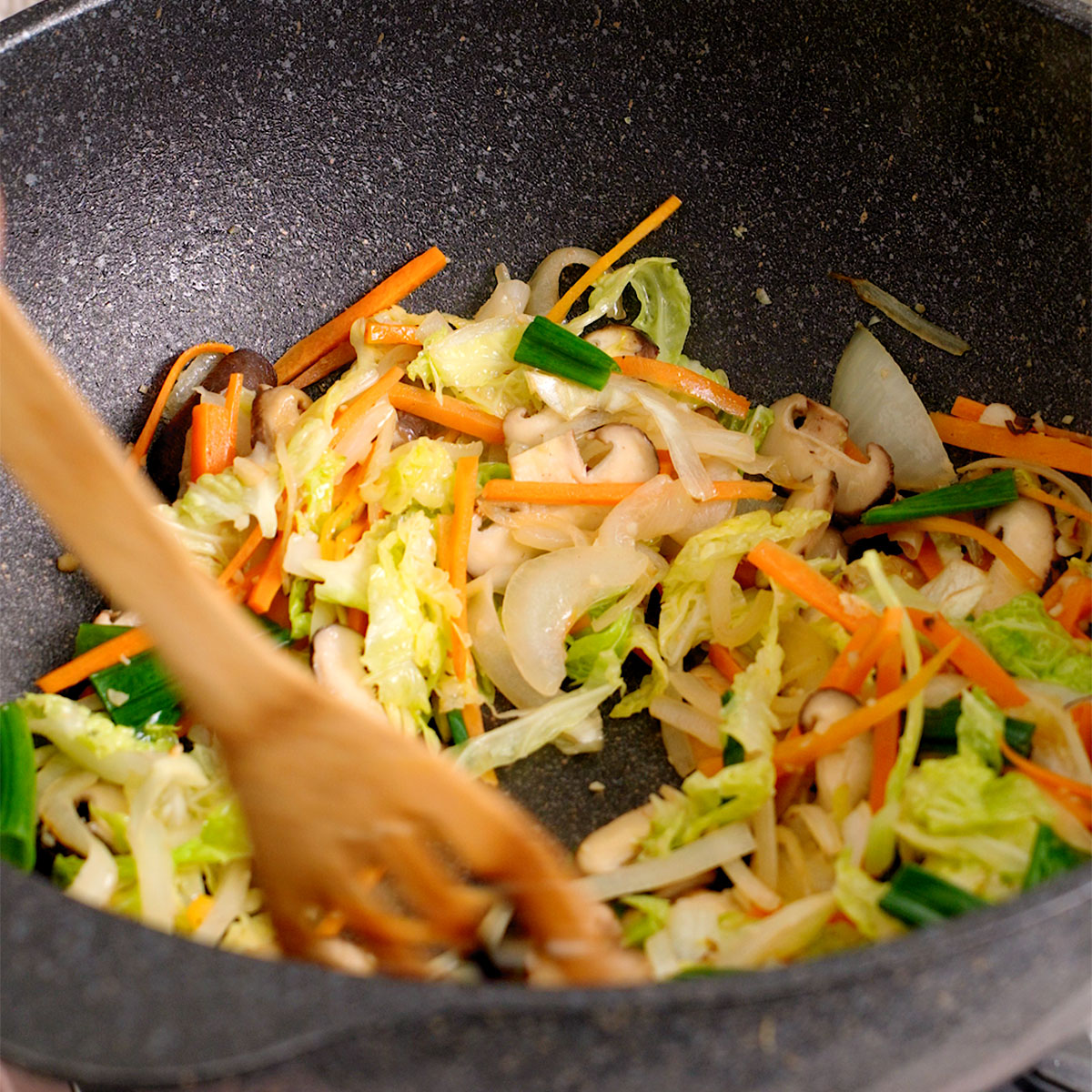 Cooking vegetables and aromatics in a large wok until softened.