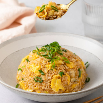 A spoonful of rice being lifted from a bowl of egg fried rice.
