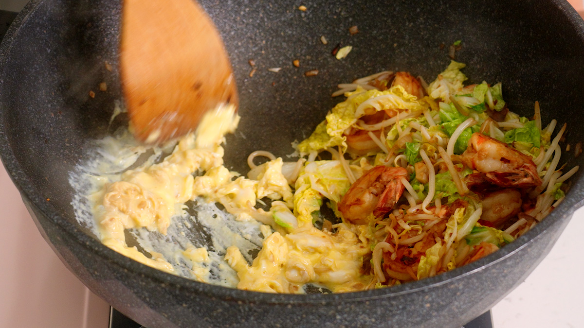 Scrambling eggs on one side of a wok before mixing together.