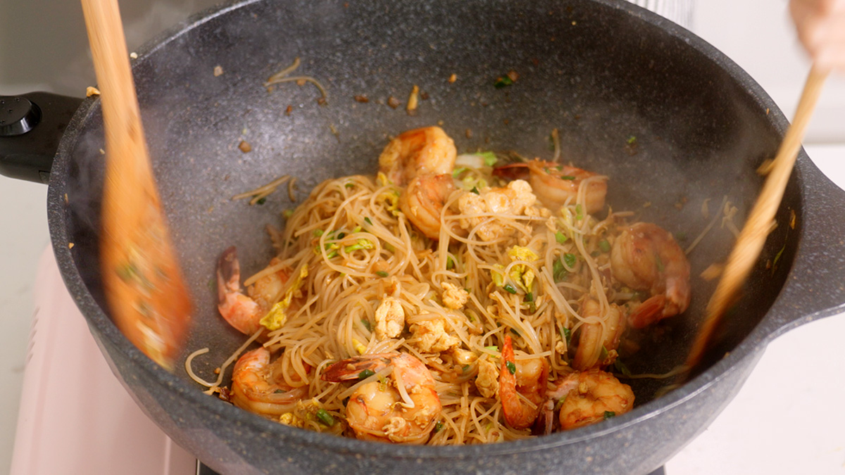 Shrimp bihun goreng fully tossed together in a large wok.