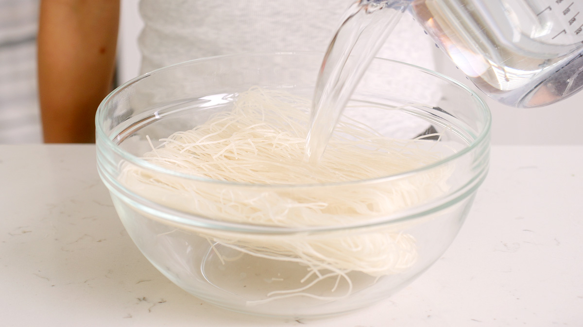 Pour hot water into a glass bowl with dried vermicelli noodles to soak them.