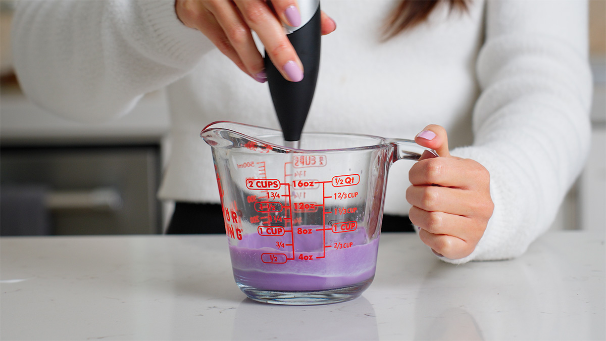 Making an ube cold foam in a mixing cup with a handheld mixer.