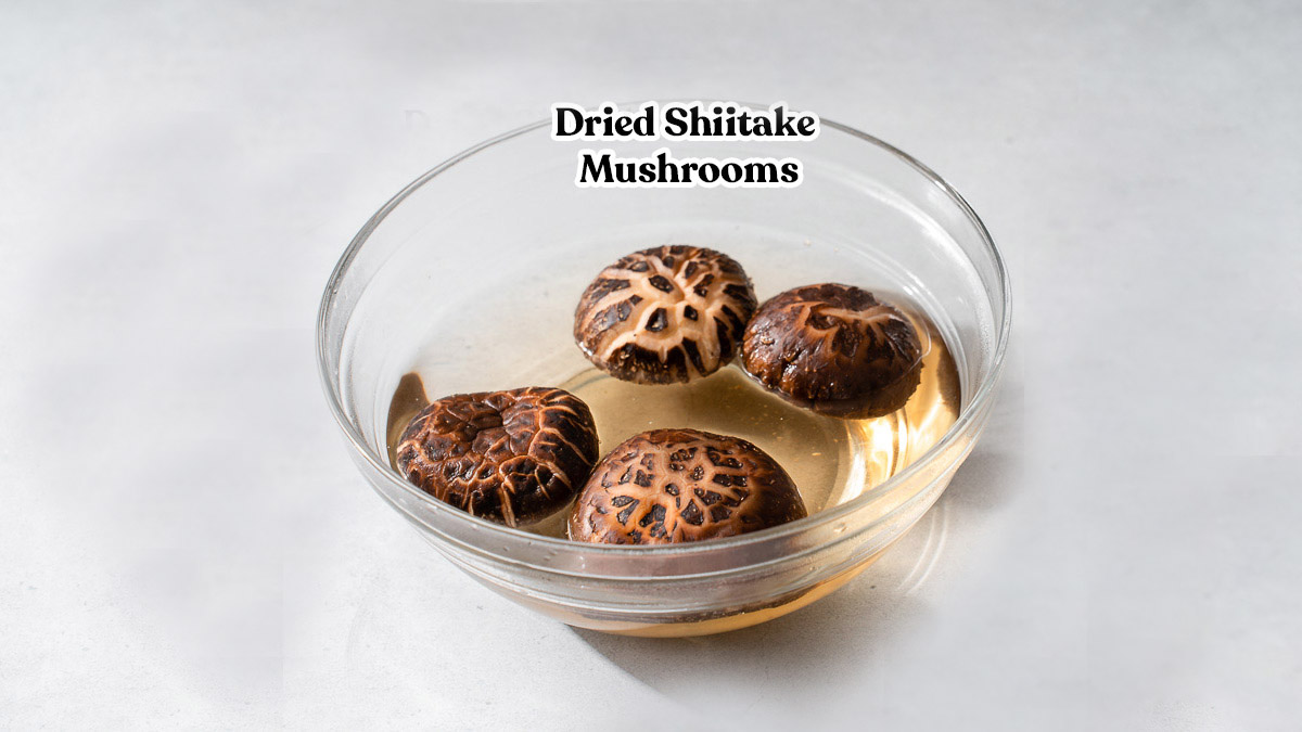 Dried shiitake mushrooms being rehydrated in a glass bowl of hot water.