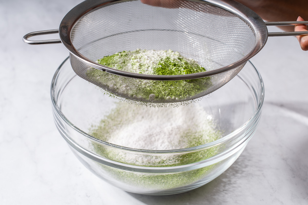 Sifting matcha and dry cake ingredients into a bowl.